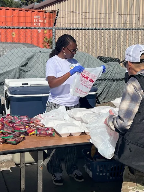 A volunteer in a Kyne Hands Foundation shirt bagging meals