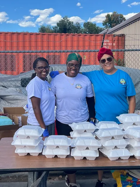 Three Kyne Hands Foundation volunteers smiling behind a table of packed meals
