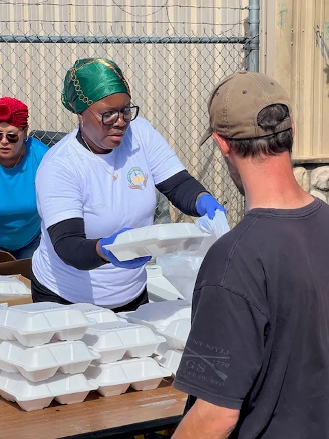 A volunteer passing a meal to a man in a cap