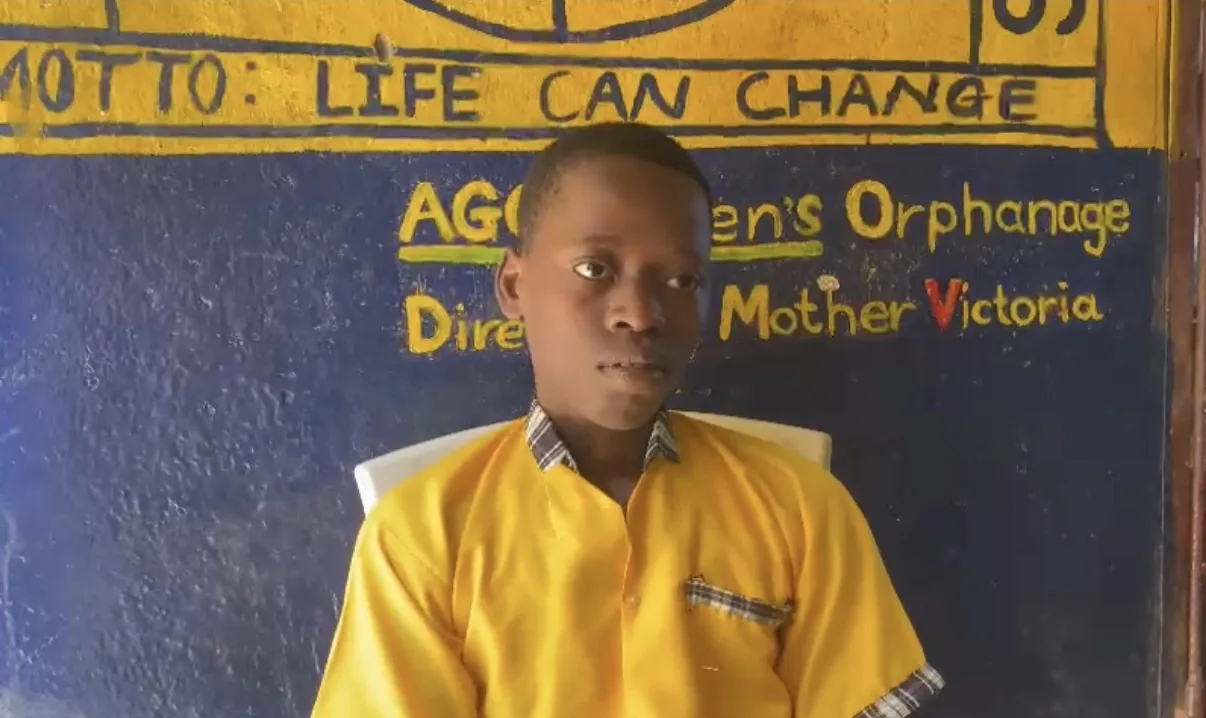A boy in a yellow shirt in front of the orphanage wall painted with the motto Life Can Change