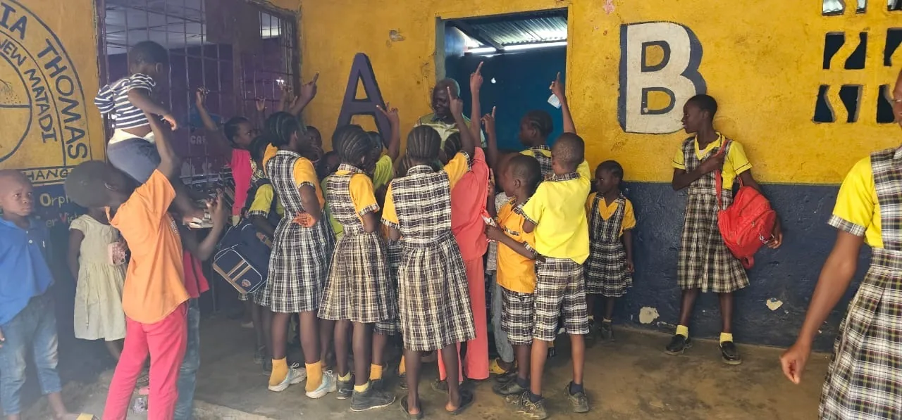 Children in plaid school uniforms raising their hands in the orphanage courtyard in Liberia