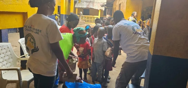 Volunteers handing out supplies to a line of children in the orphanage courtyard