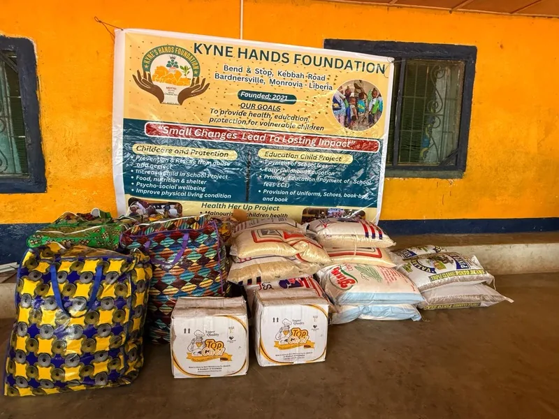 Bags of rice and supplies stacked under a Kyne Hands Foundation banner, ready for distribution in Liberia