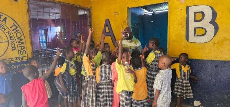 Children in school uniforms with their hands raised in front of a classroom wall