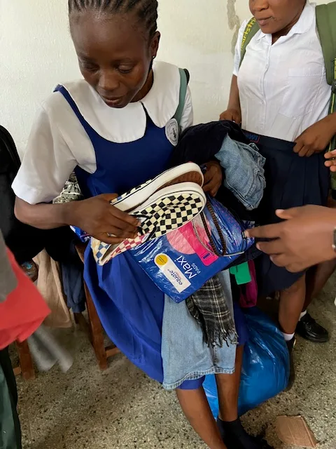 A schoolgirl in Liberia holding the shoes, clothes and sanitary pads Kyne Hands Foundation gave her