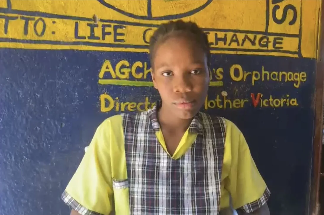 A girl in her school uniform in front of the orphanage wall, painted with the motto Life Can Change